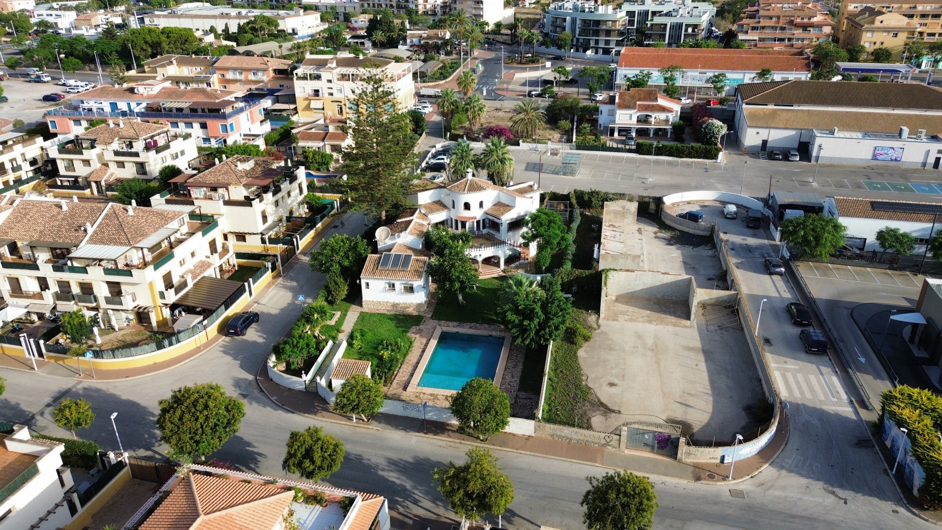 Aerial view of the villa with blue pool surrounded by gardens and urban buildings in Jávea.