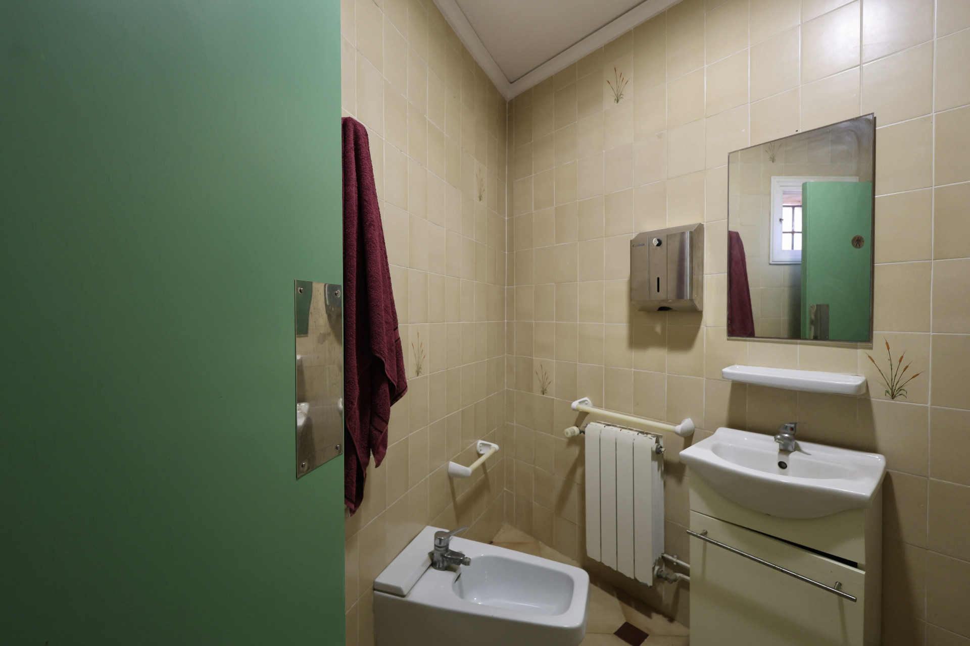 Bathroom featuring cream tiles, a white bidet, and a green door.