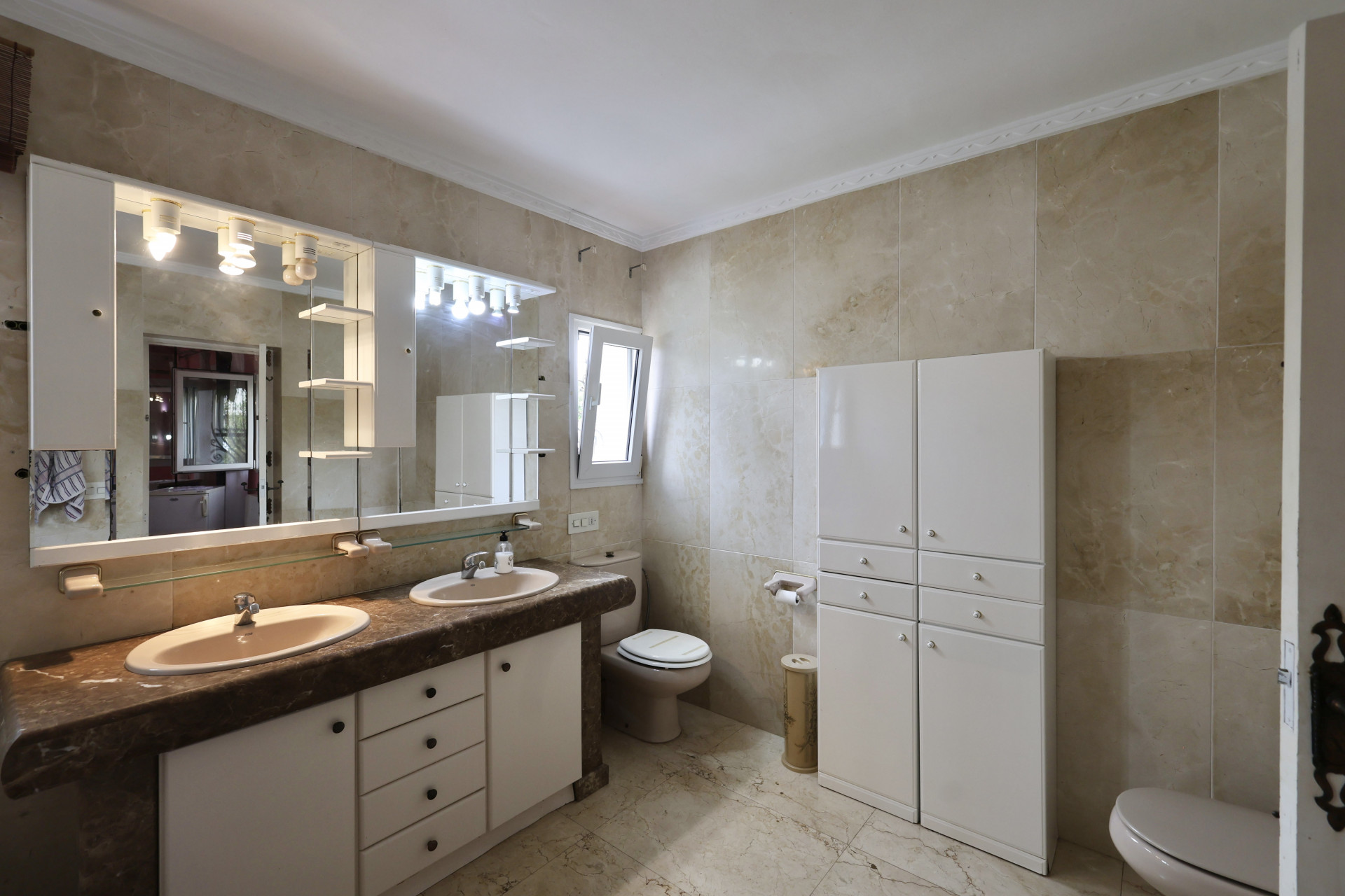 Bathroom with double sink, marble countertop, and white cabinets.