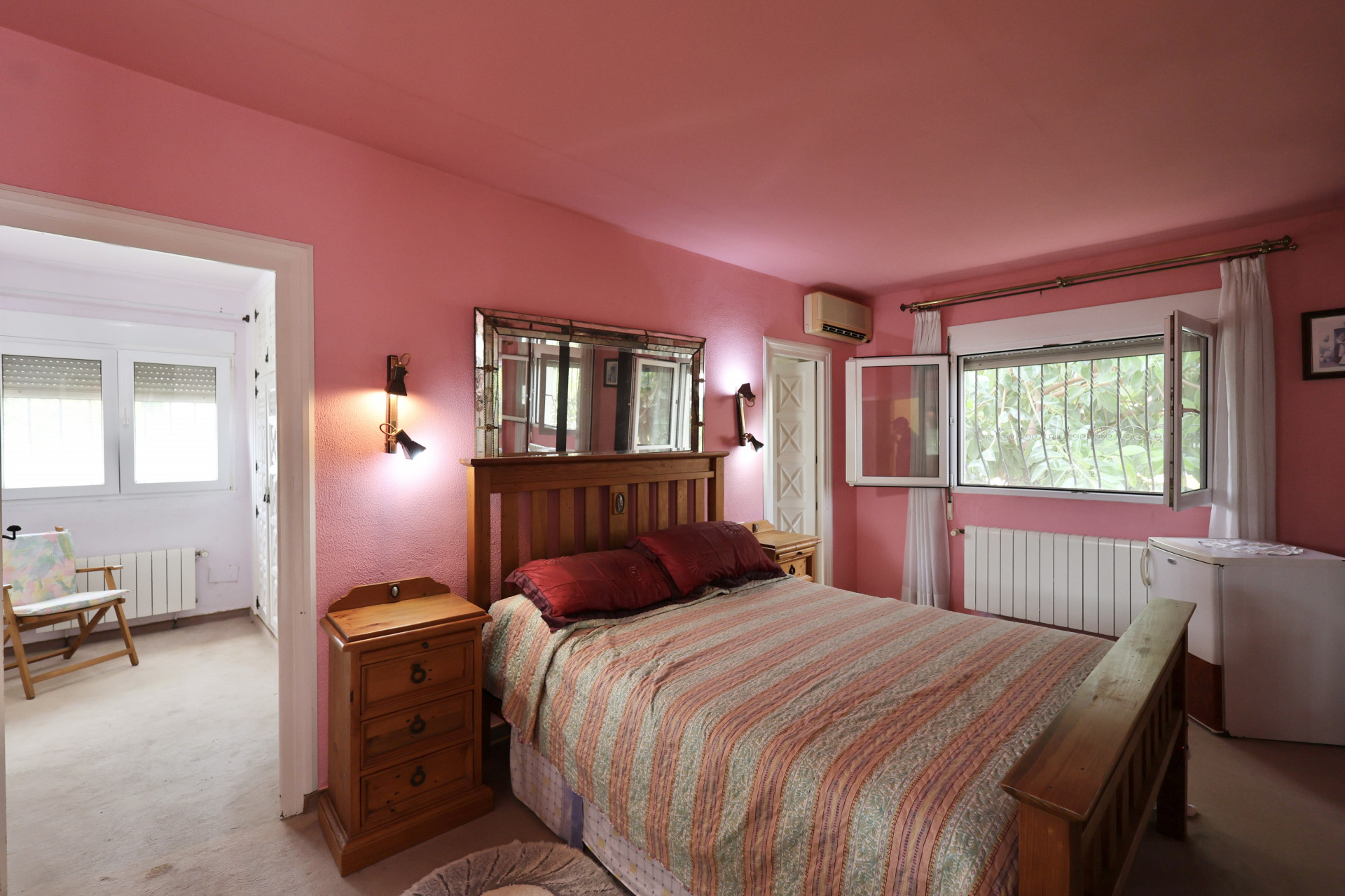 Bedroom with pink walls, wood bed frame, and sconce-lit mirror. Renovation needed.
