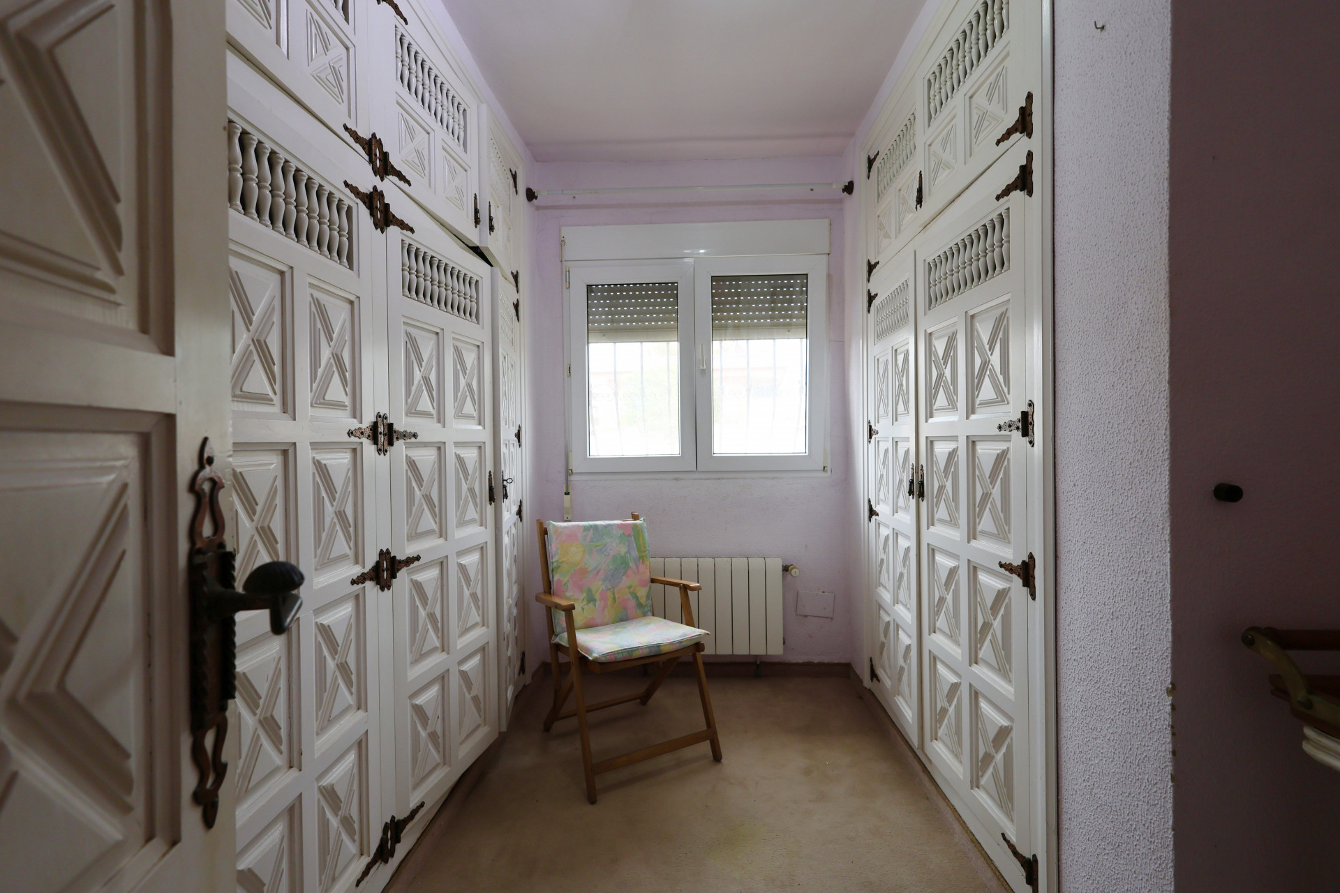 Dressing room with white built-in wardrobes and iron hardware, lit by a window.