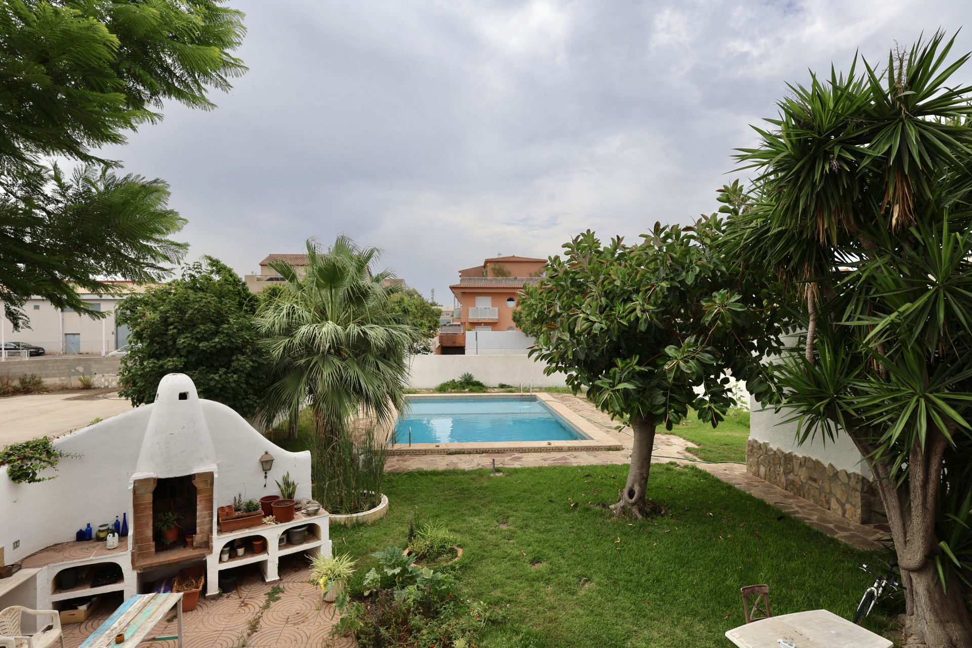 Garden view with pool, brick barbecue, and lush vegetation in Jávea.