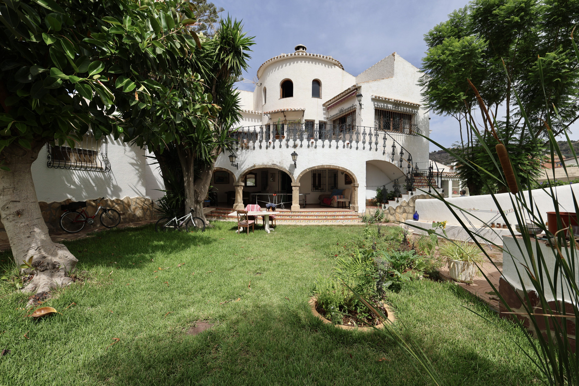 Lawn view of the villa's white facade with arches and an outdoor dining table.