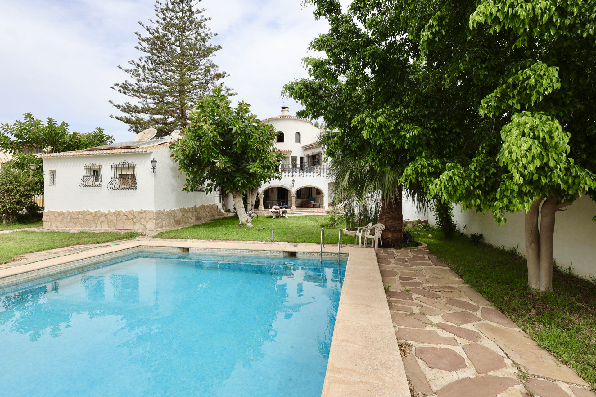 View of the turquoise pool with stone border, surrounded by lush green lawn and vegetation.