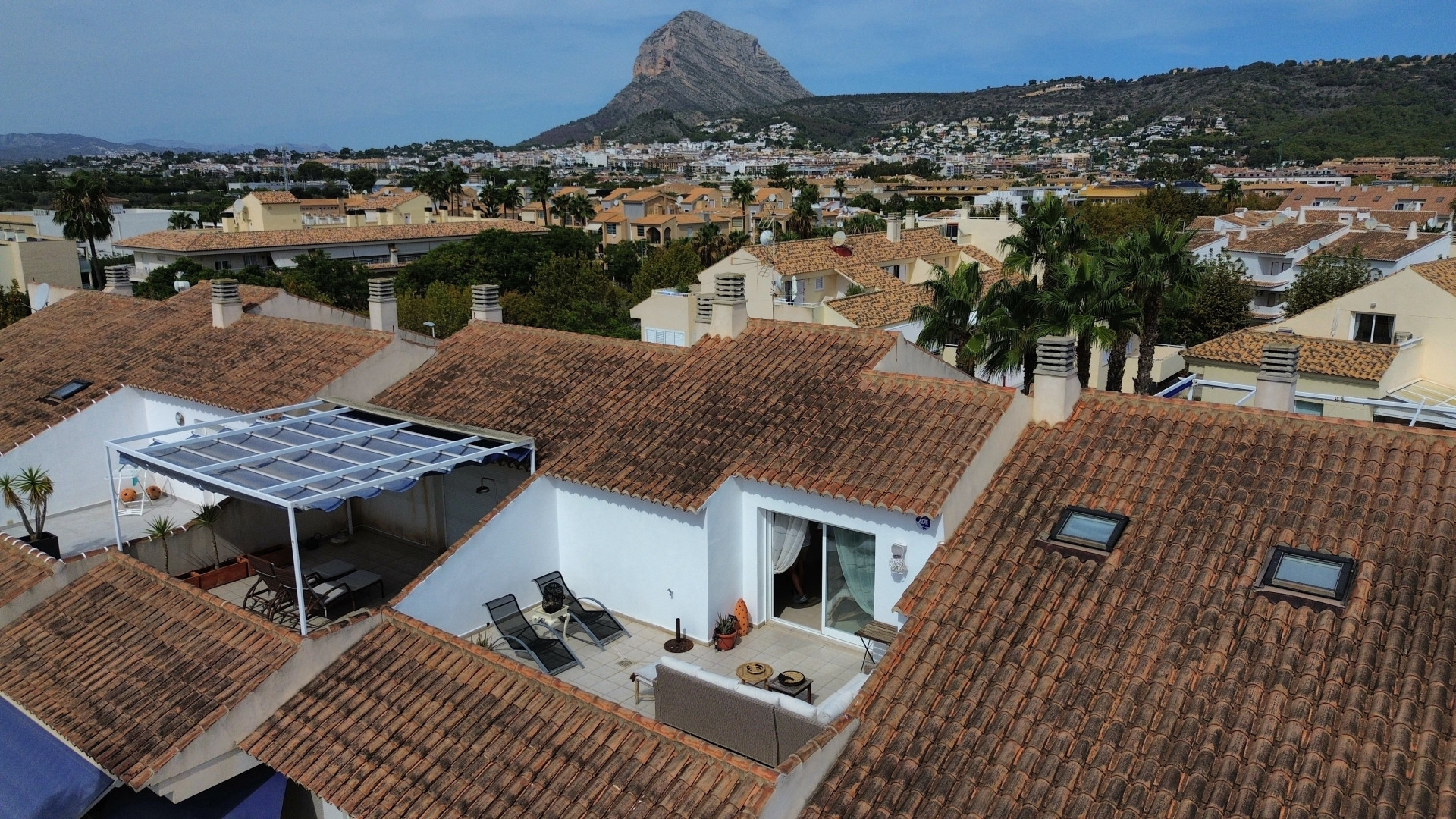 Aerial view of the solarium terrace with awning and outdoor furniture, surrounded by tiled roofs.
