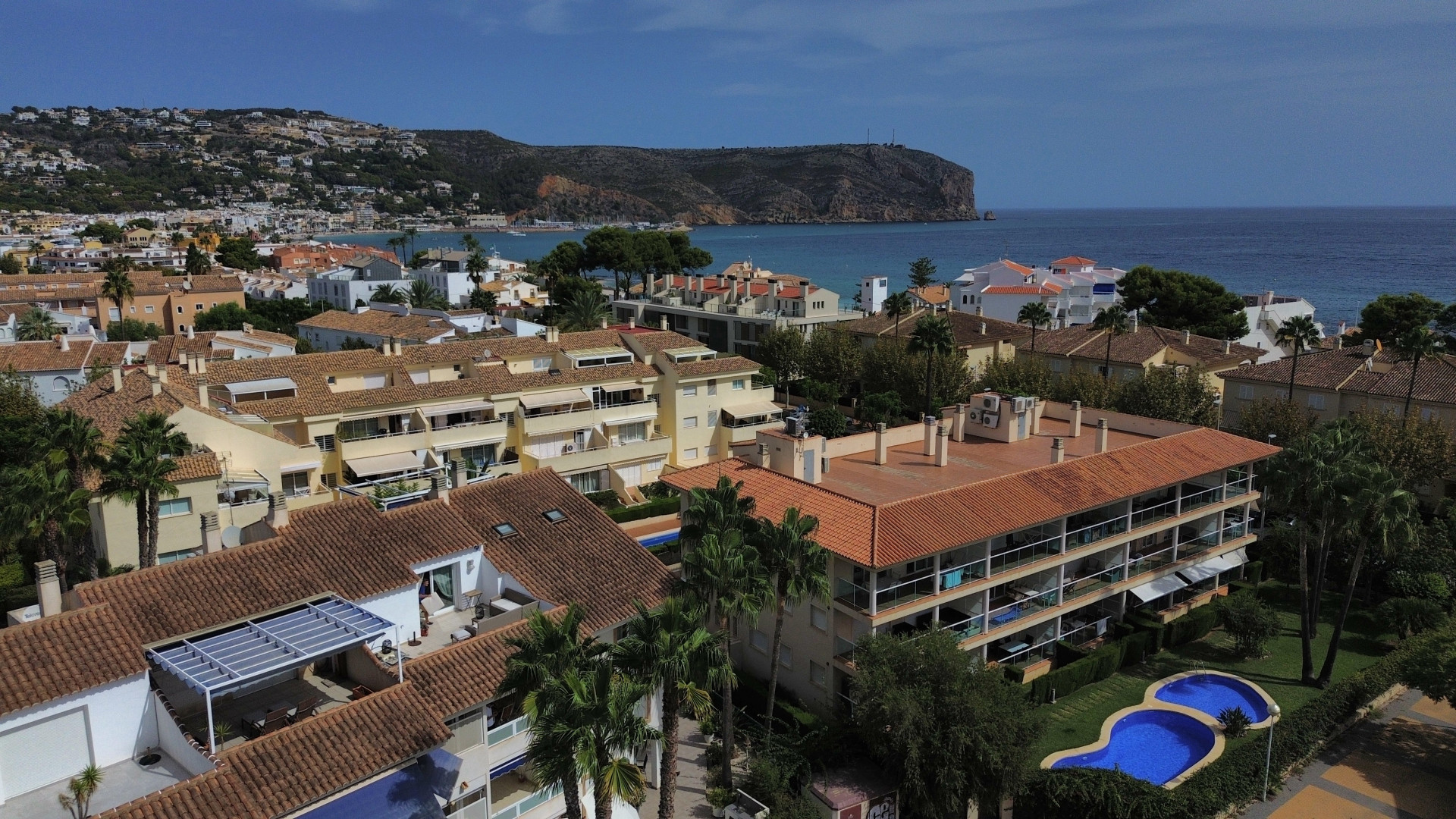 Aerial view of the urbanization with a pool and residential buildings with red roofs near the Jávea coast.