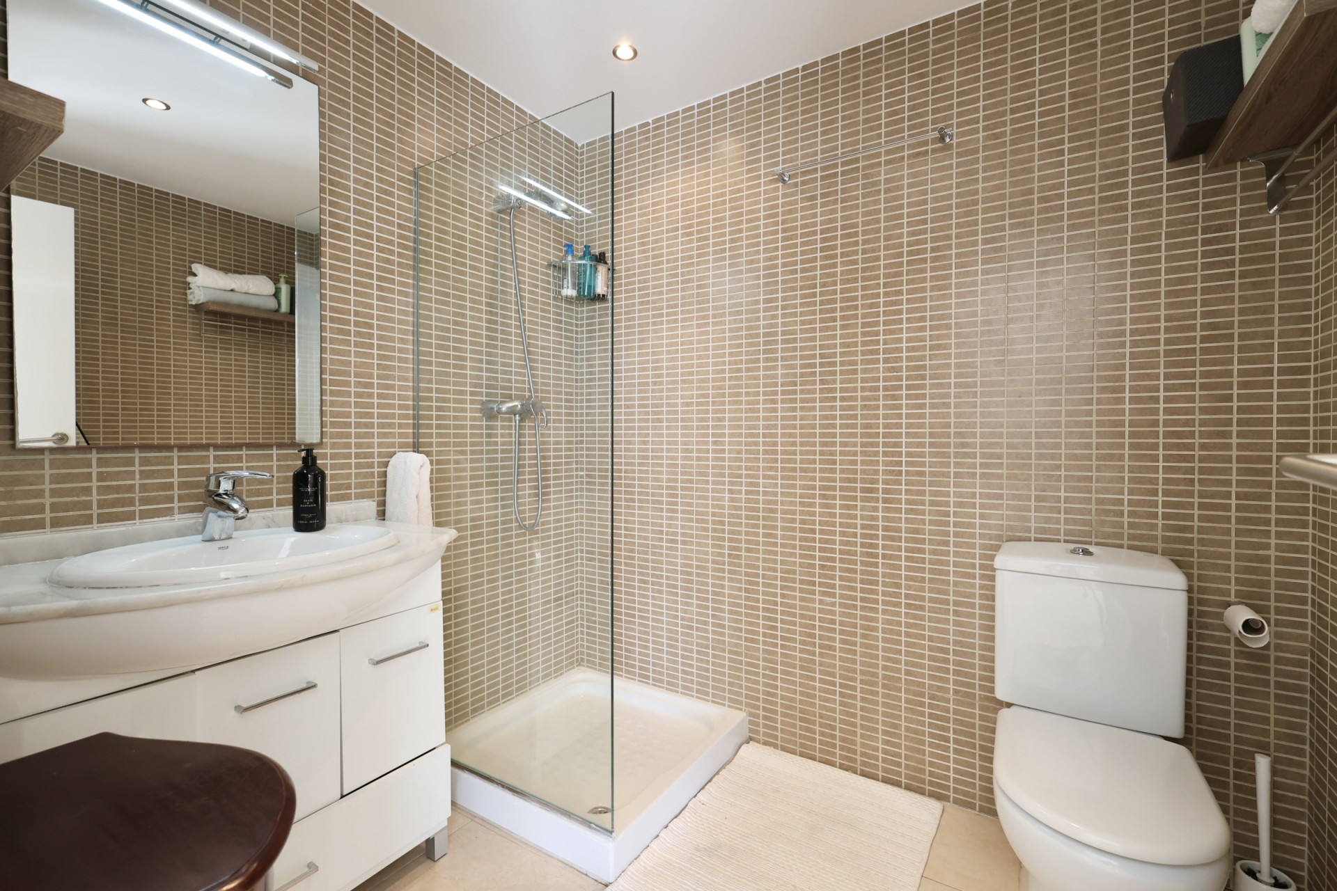 Bathroom featuring sand-toned tiled walls, a glass-enclosed shower, and a vanity with a marble countertop.