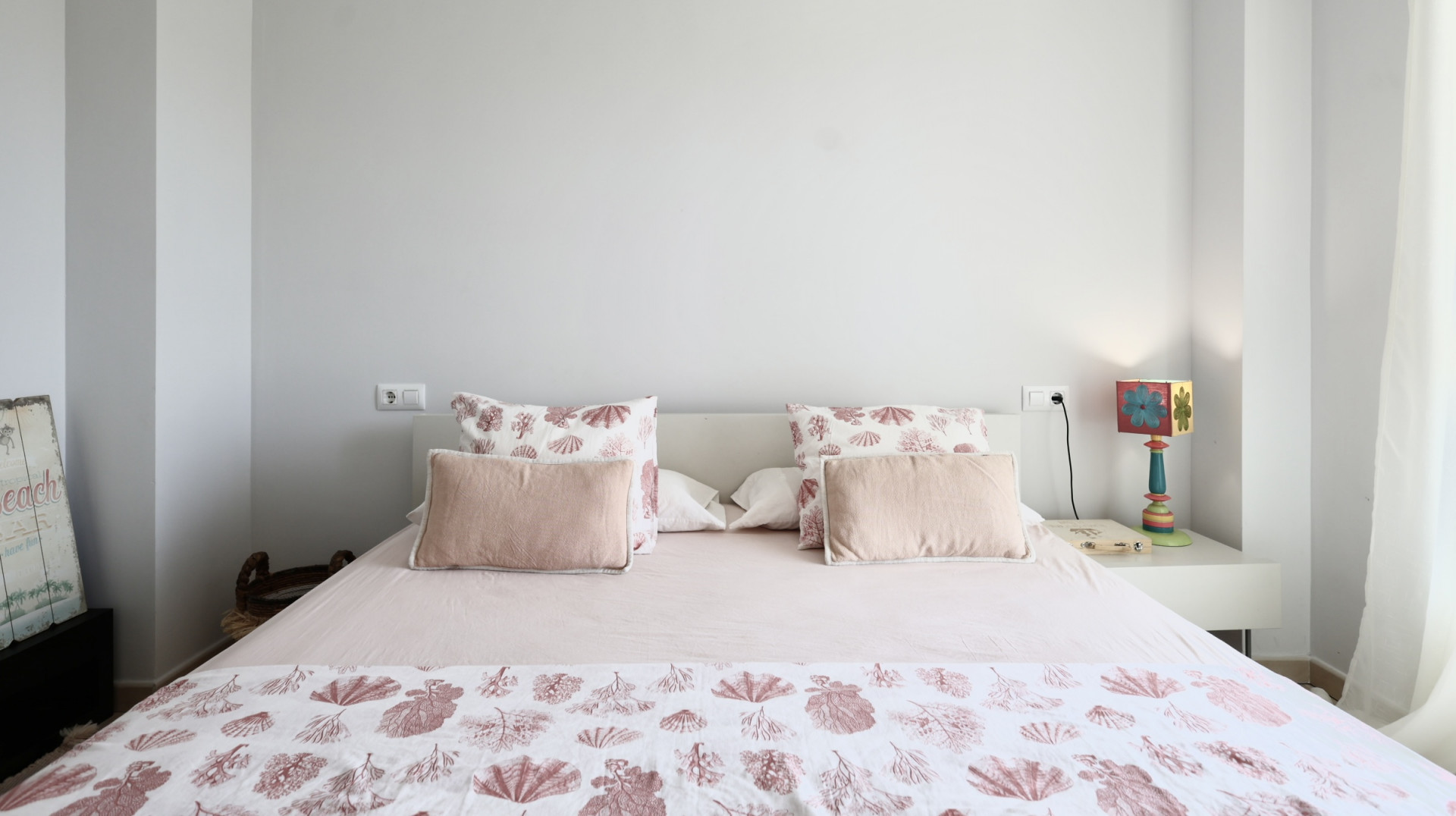 Bright bedroom featuring a double bed, marine-themed bedding, and a white bedside table with a decorative lamp.