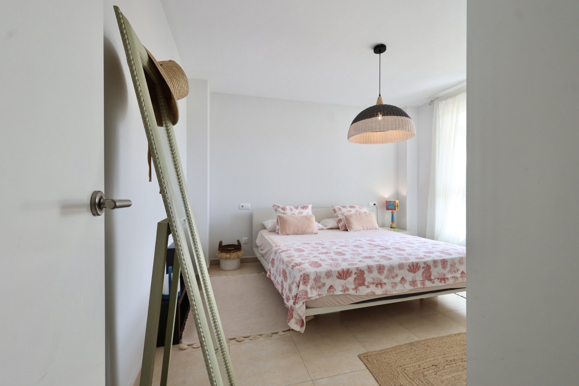 Bright bedroom featuring a double bed with marine-themed bedding and a wicker pendant lamp.