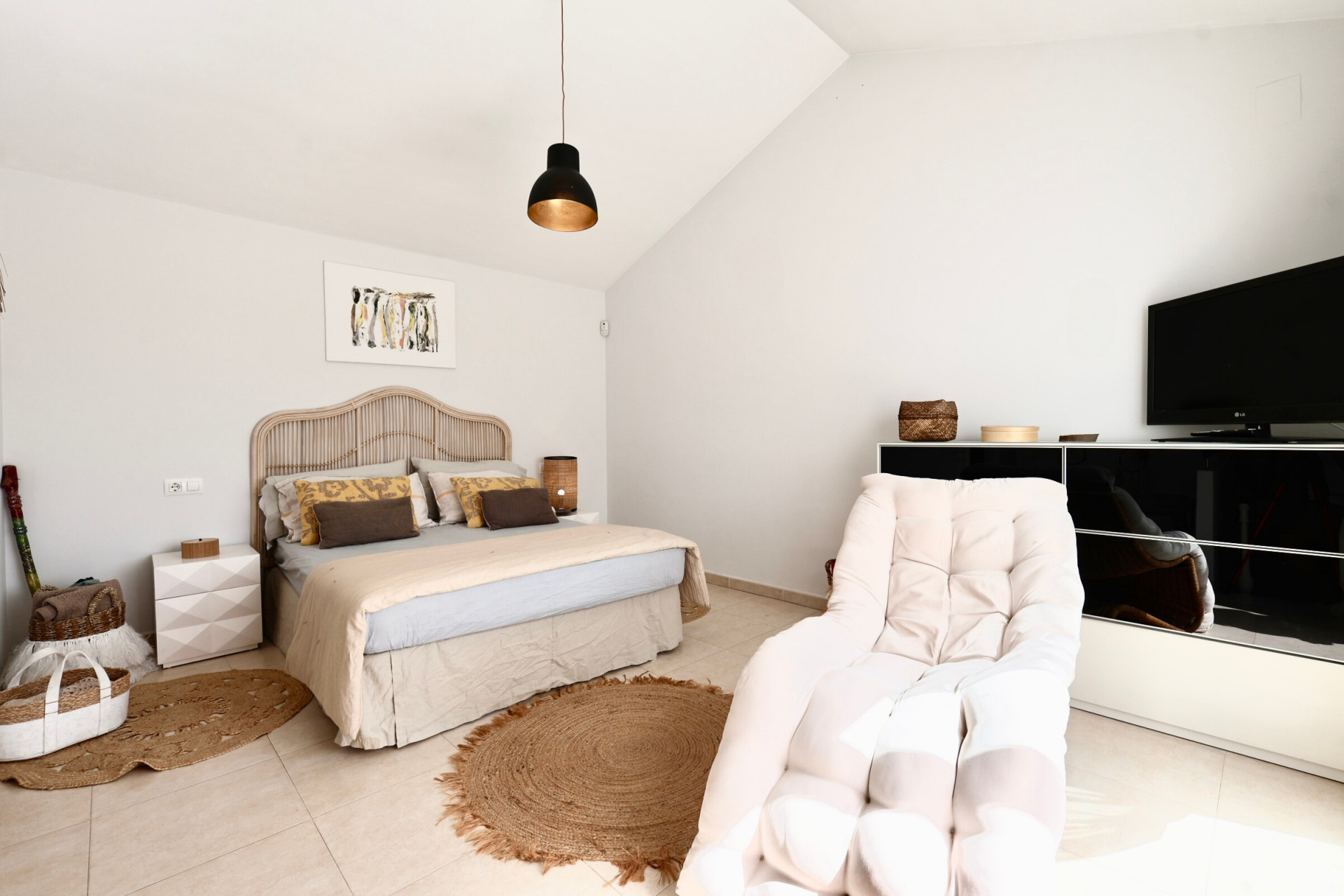 Bright bedroom featuring a rattan bed, jute rug, and armchair next to a black TV stand.