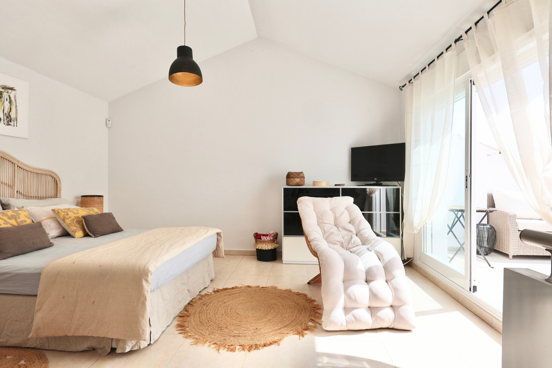 Bright bedroom featuring a rattan bed, jute rug, and terrace access.