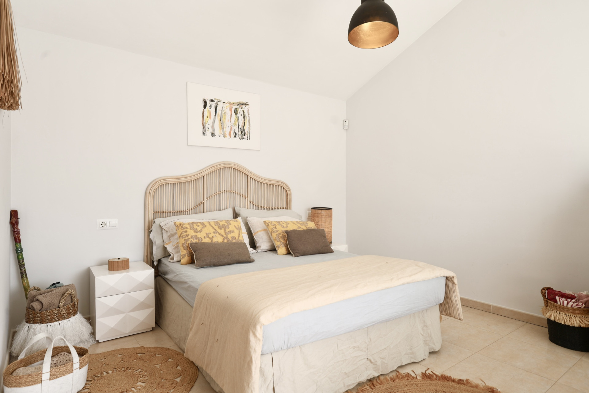 Bright bedroom featuring a rattan bed, round jute rug, and minimalist decor.