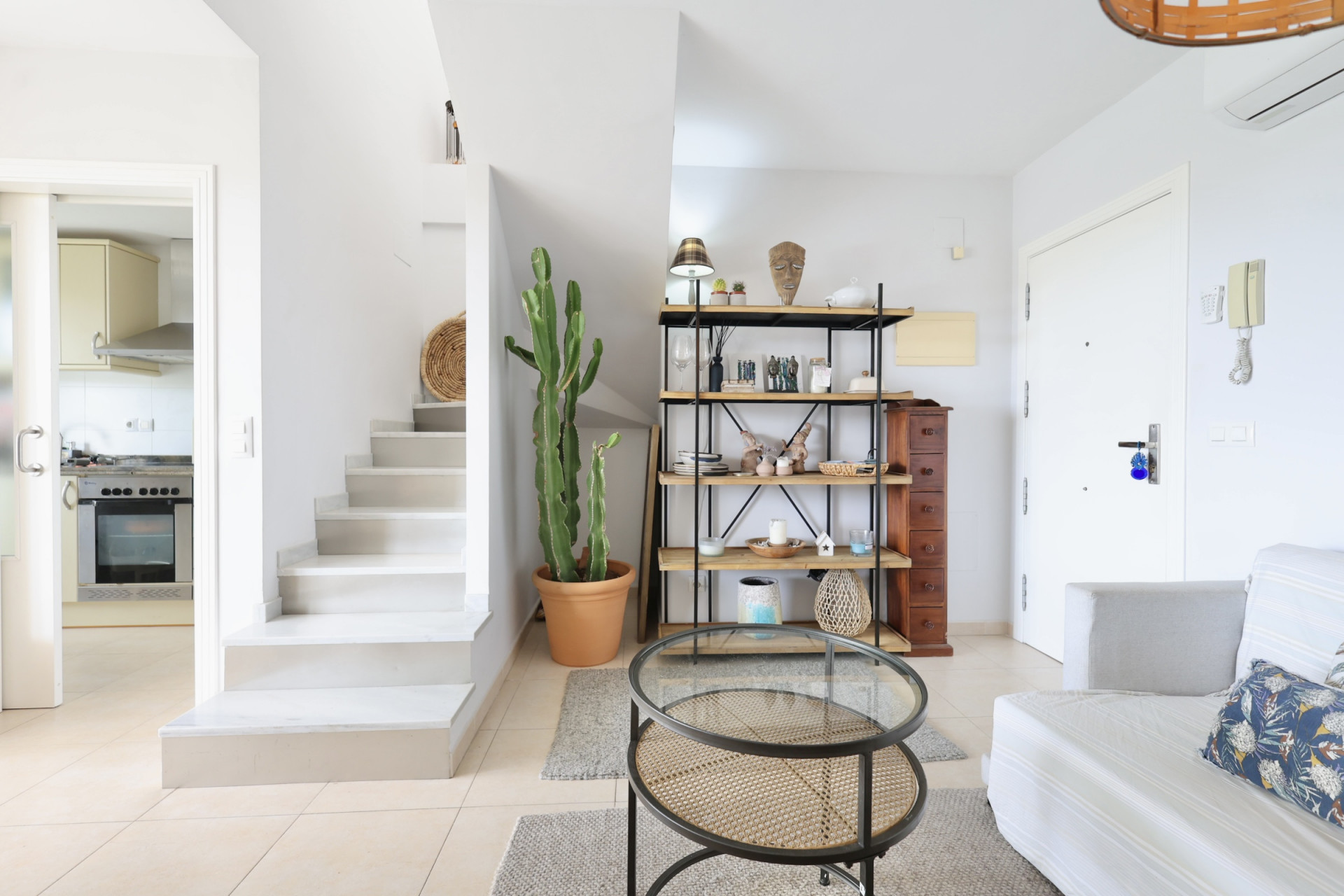 Bright interior featuring a white staircase, wood and metal shelving, and a rattan coffee table.