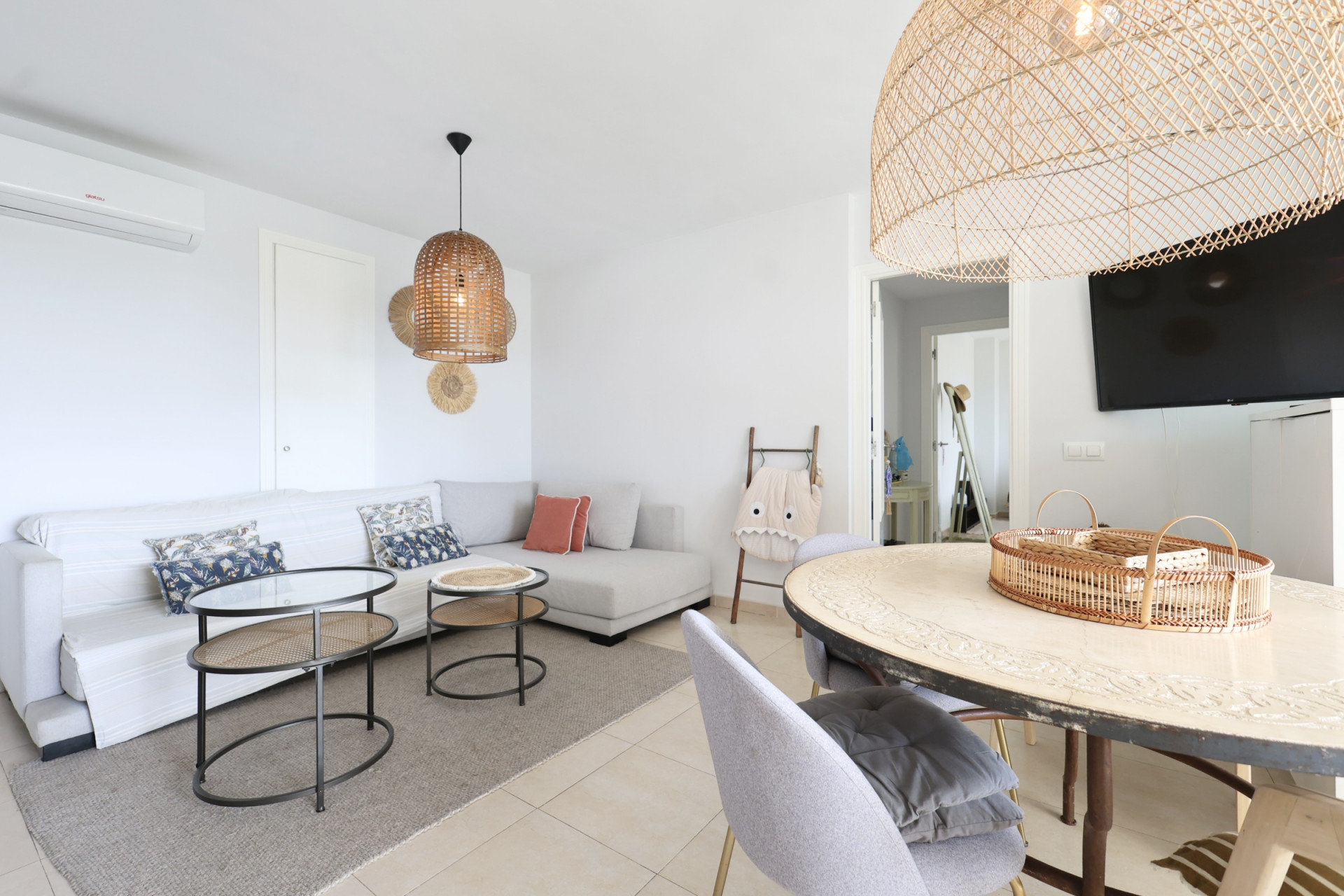 Bright living-dining room featuring a sectional sofa, wicker lamps, and a designer coffee table.