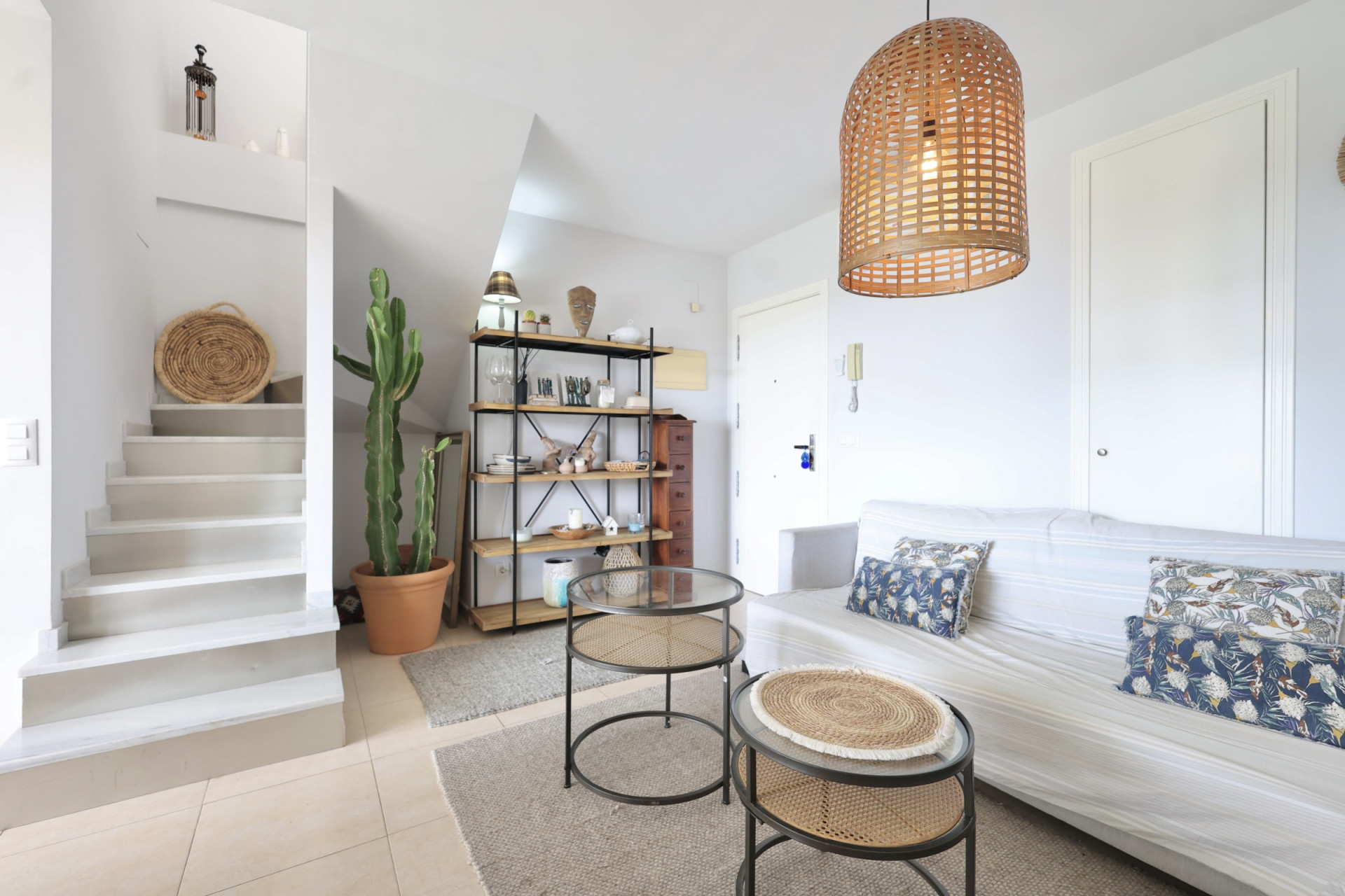 Bright living room with staircase to the duplex, minimalist decor, and a wicker pendant lamp.
