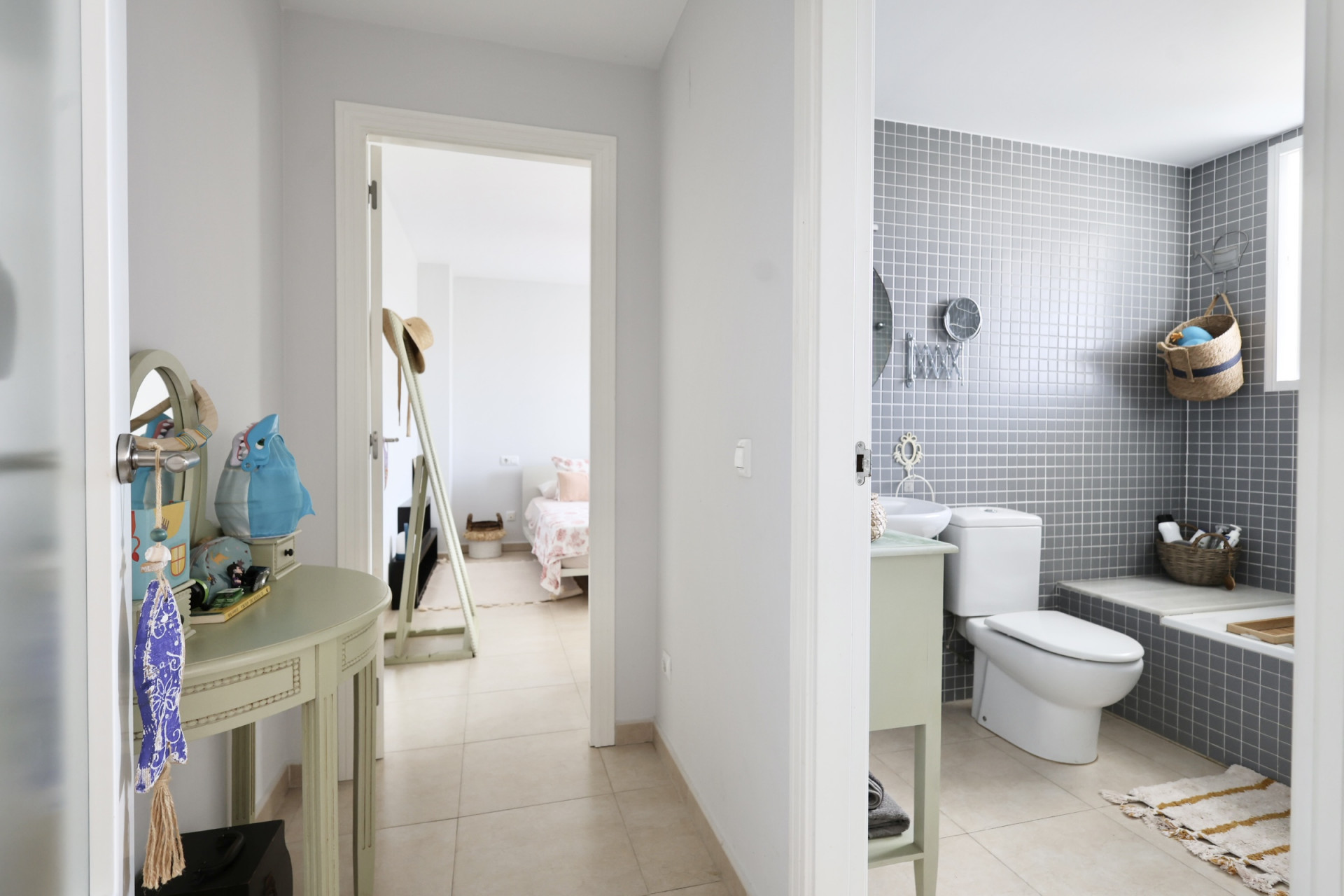 Hallway detail with decorative console table and view into bathroom with gray tiles and bedroom in the background.