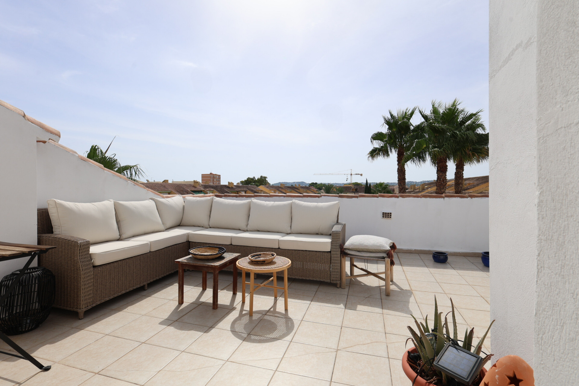Sun-drenched tiled terrace featuring a wicker sectional sofa and palm tree views.