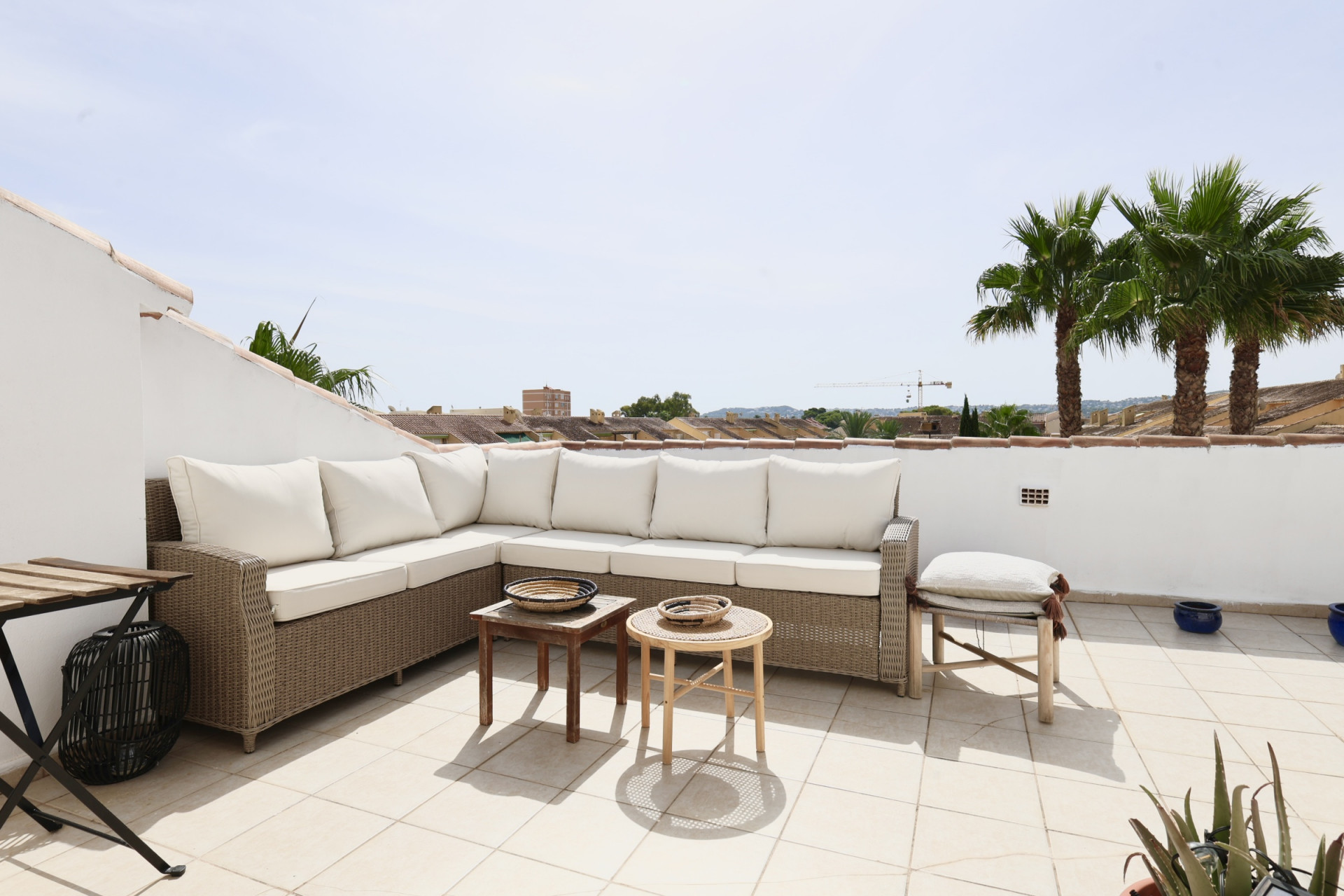 Terrace featuring a wicker sectional sofa with white cushions, overlooking palm trees and rooftops.
