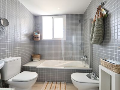 Bathroom featuring gray tiled walls, a bathtub with a glass screen, and wicker decorative elements.
