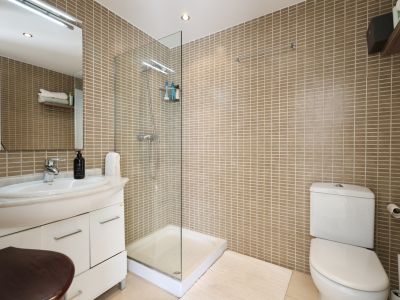 Bathroom featuring sand-toned tiled walls, a glass-enclosed shower, and a vanity with a marble countertop.