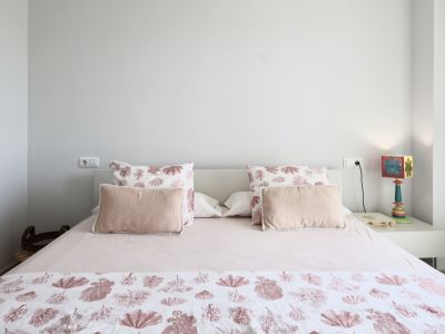 Bright bedroom featuring a double bed, marine-themed bedding, and a white bedside table with a decorative lamp.