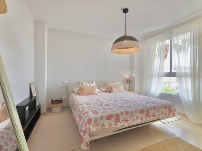 Bright bedroom featuring a double bed, patterned bedding, and a wicker pendant lamp.