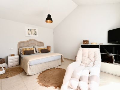 Bright bedroom featuring a rattan bed, jute rug, and armchair next to a black TV stand.