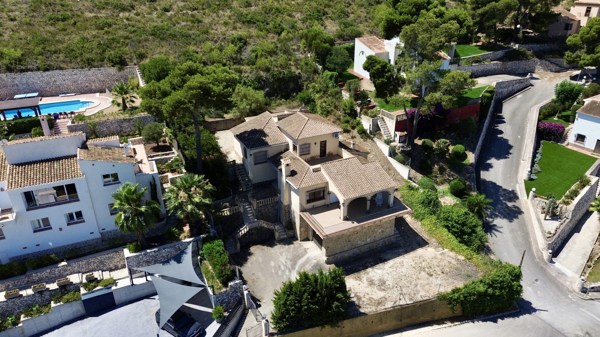 Aerial view of the multi-level villa featuring traditional tiled roofs, multiple terraces, and sloping garden areas, integrated into Mediterranean vegetation.