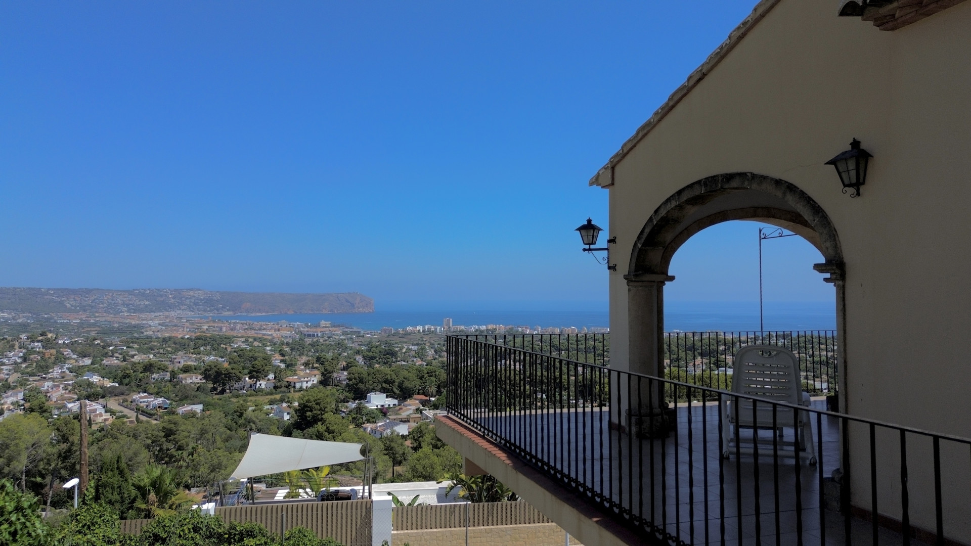 Covered terrace offering expansive sea, town, and landscape views, featuring an architectural archway and black metal railing.