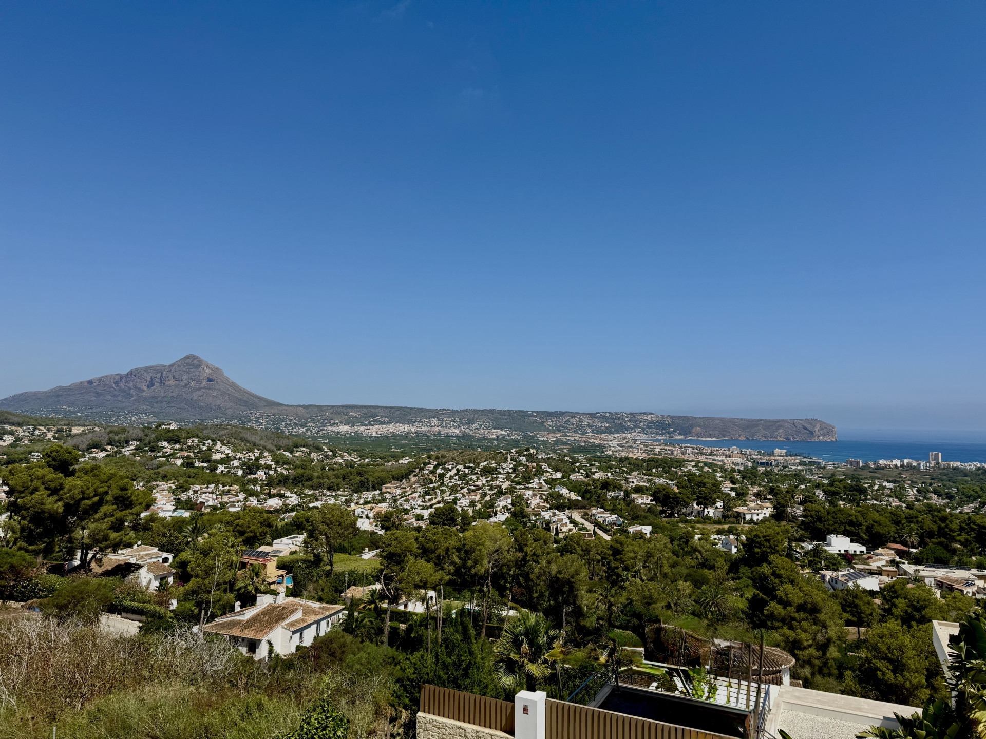 Panoramic view of Jávea featuring the majestic Montgó mountain, the Mediterranean Sea, and the lush, tree-lined urban landscape under a clear sky.