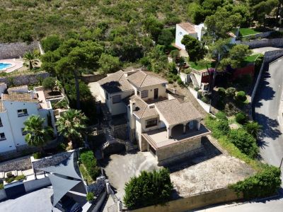 Aerial view of the multi-level villa featuring traditional tiled roofs, multiple terraces, and sloping garden areas, integrated into Mediterranean vegetation.