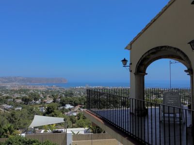 Covered terrace offering expansive sea, town, and landscape views, featuring an architectural archway and black metal railing.