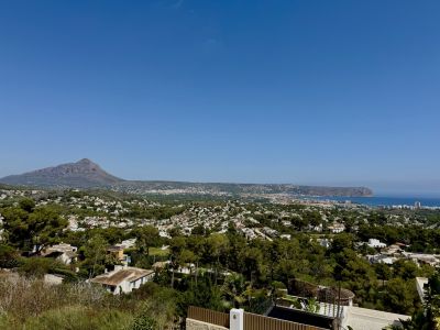 Panoramic view of Jávea featuring the majestic Montgó mountain, the Mediterranean Sea, and the lush, tree-lined urban landscape under a clear sky.
