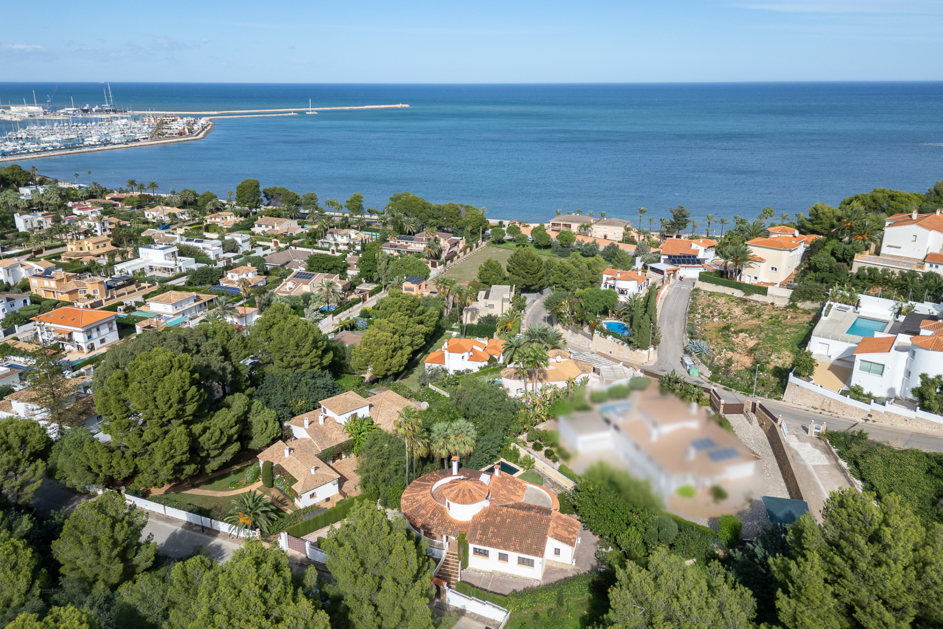 Aerial view of Dénia's residential area, showcasing villas, lush greenery, and the marina adjacent to the Mediterranean Sea.