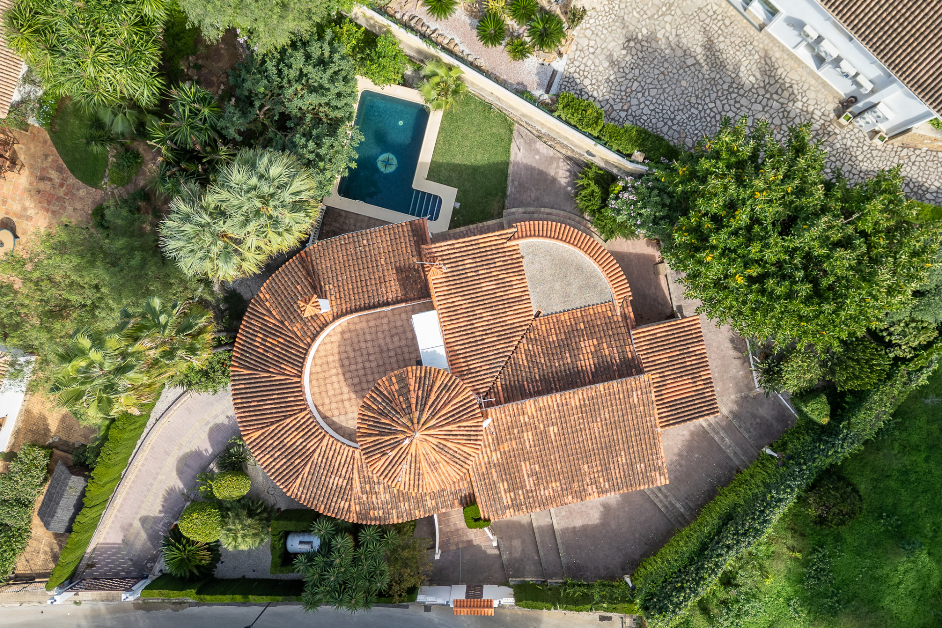 Aerial view showcasing the villa's distinctive red-tiled roofs, private swimming pool with a compass design, and surrounding lush Mediterranean gardens.