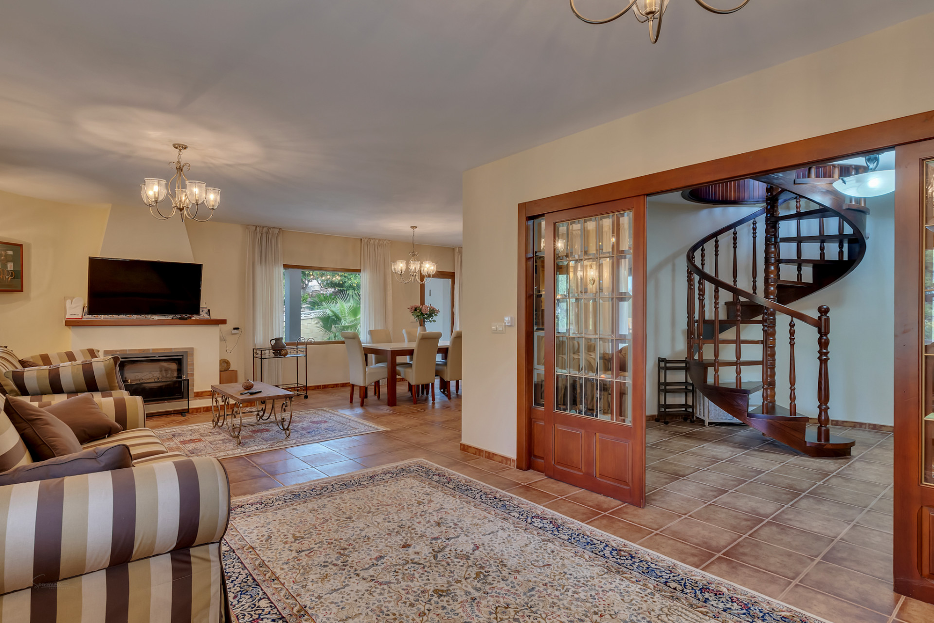 Open-plan living and dining area featuring a fireplace, tiled floors, and a distinctive wooden spiral staircase accessed via glass-paneled sliding doors.