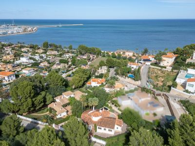 Aerial view of Dénia's residential area, showcasing villas, lush greenery, and the marina adjacent to the Mediterranean Sea.