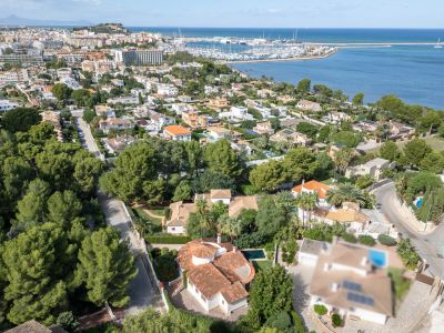 Aerial view showcasing the villa with its distinct red-tiled roof and private pool, nestled within a green residential area of Dénia, overlooking the marina and sea.