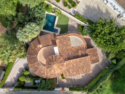 Aerial view showcasing the villa's distinctive red-tiled roofs, private swimming pool with a compass design, and surrounding lush Mediterranean gardens.