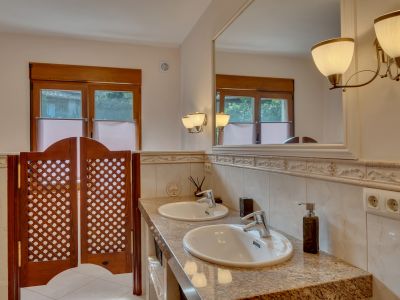Bathroom with double granite vanity, two sinks, and a large framed mirror with elegant wall sconces. Features wooden windows and lattice saloon doors.