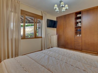 Bedroom featuring a double bed, integrated wooden wardrobes, and a window overlooking a landscaped wall. Includes a wall-mounted TV and white dresser.