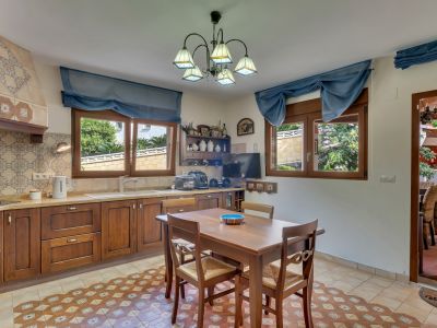 Functional kitchen featuring dark wood cabinetry, decorative tiled backsplash, and patterned floor tiles. Two windows offer garden views, complemented by a wooden dining table.