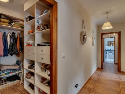 Hallway with an integrated open wardrobe featuring white shelving and drawers, terracotta floor tiles, and wooden door frames.