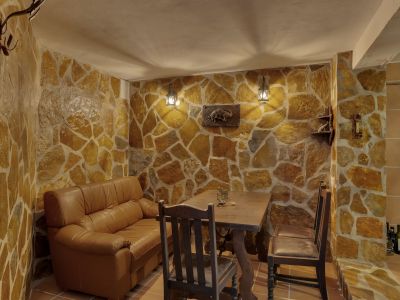 Interior space featuring irregular stone-clad walls and tiled flooring. Furnished with a leather sofa, rustic wooden table, and warm lantern wall lights.
