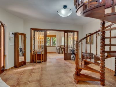 Main entrance featuring a dark wooden spiral staircase and terracotta tiled flooring. Wooden and glass sliding doors open to a bright adjoining room.