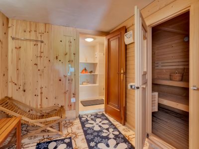 Relaxation area featuring light wood-paneled walls, tiled flooring, and direct access to a pine wood sauna. Includes a wooden lounge chair and an adjacent utility space with shelving.
