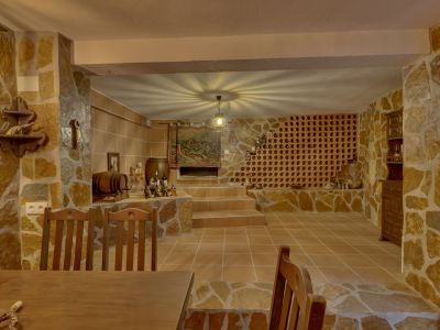 Rustic cellar featuring natural stone walls, terracotta floor tiles, and a prominent built-in wine rack. A central light fixture creates a unique ceiling pattern, complementing the traditional decor and wooden elements.