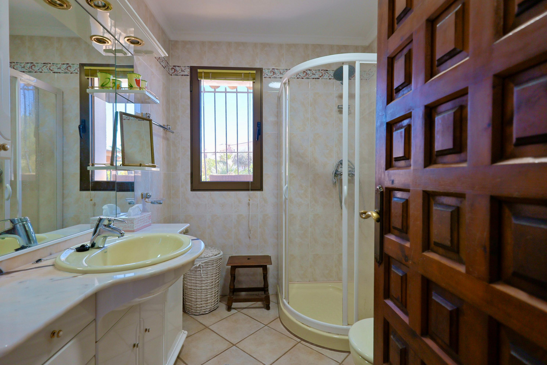 Bathroom detail with yellow sink, corner shower, and carved wooden door.