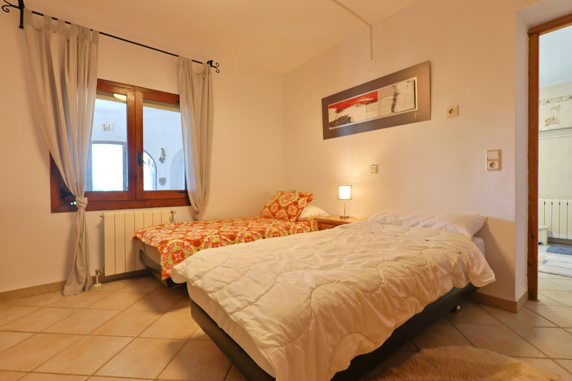 Bright bedroom featuring twin beds, a wooden window frame, and tiled flooring.