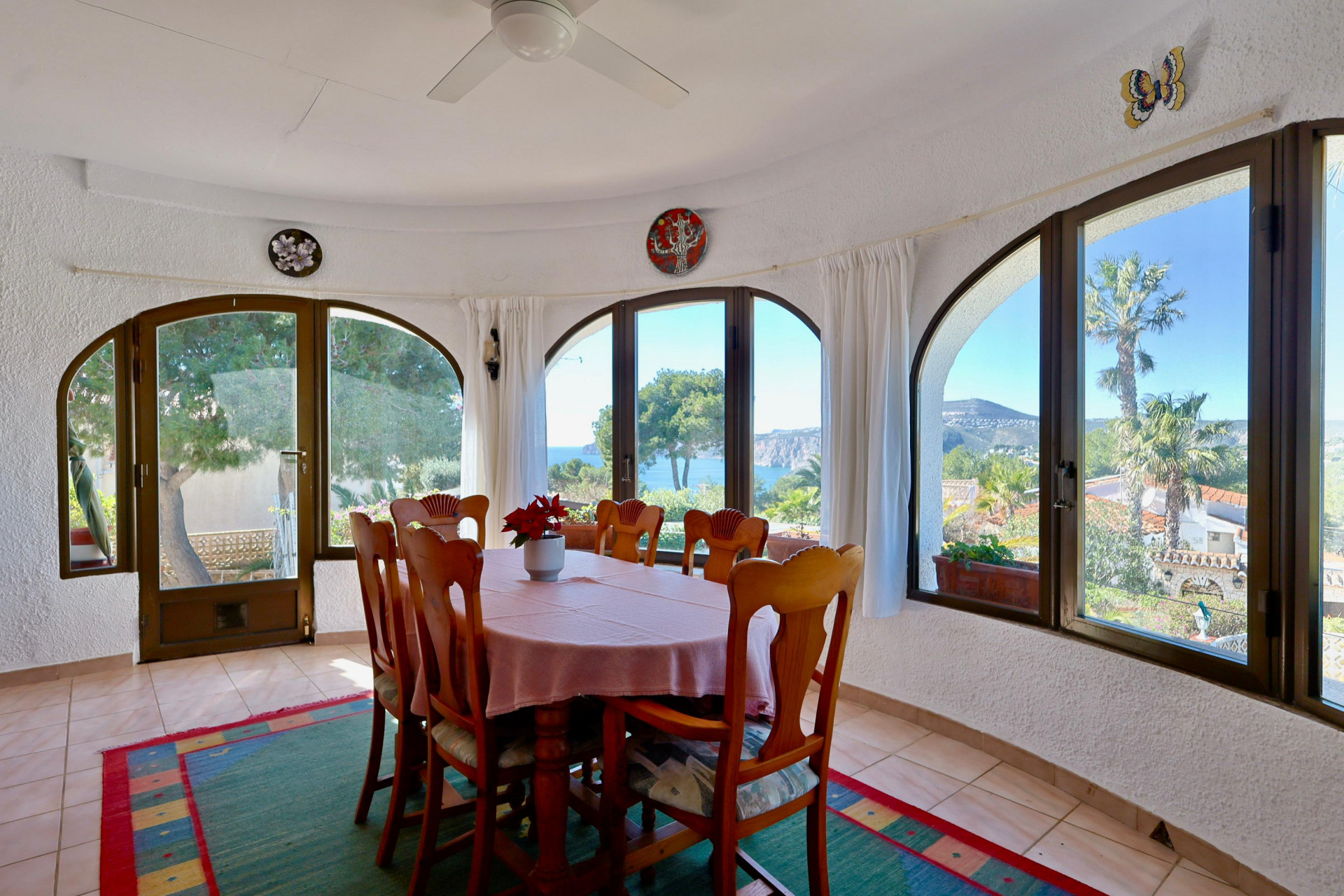 Bright dining room with sea views, surrounded by arched windows and rustic decor.